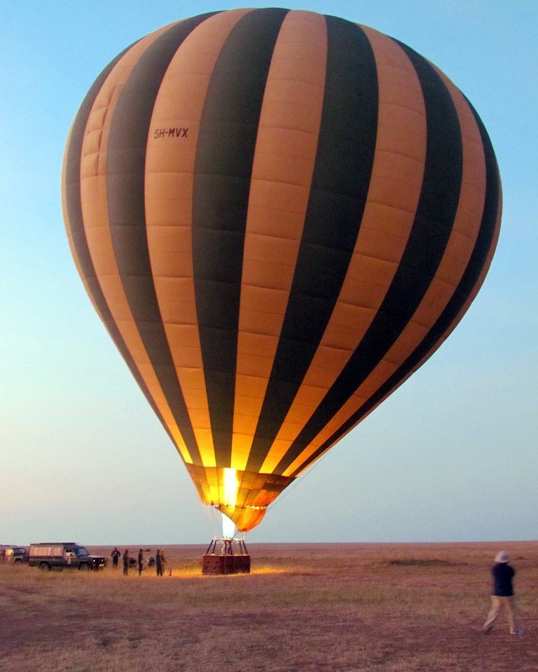 A hot-air balloon lifting off over the savannah at sunrise